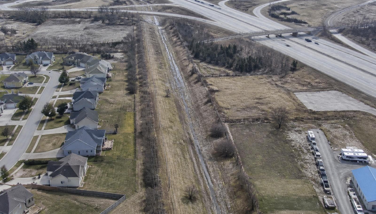 Aerial view of a drainage and utility easement corridor crossing suburban parcels beside a highway interchange